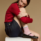 Le modèle porte des chaussettes courtes blanches à rayures rouges et bleues pour femme, style marinière.