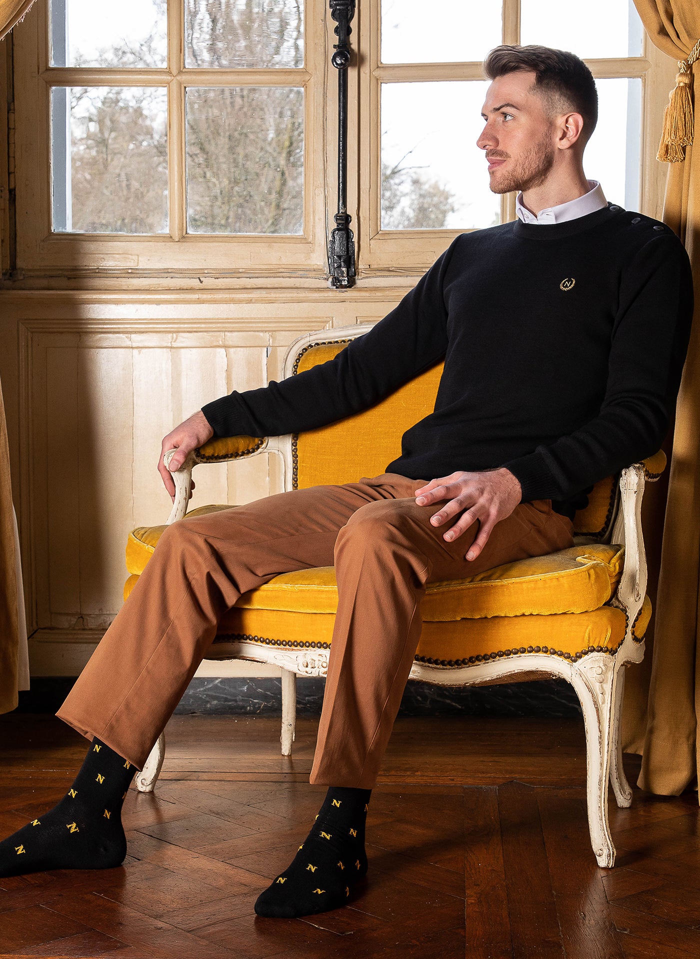 homme assis dans un fauteuil, portant un pull napoléon noir et une paire de chaussettes Napoléon noires Maison Broussaud