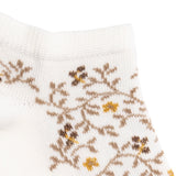 Détail du motif floral marron et jaune sur chaussette femme blanche.